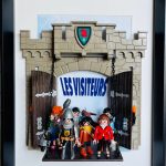 Plusieurs figurines miniatures variées (un chevalier en armure, une femme en veste rouge, un homme à la chemise orange, et d’autres personnages) sortant par des grandes portes en bois d’un château gris, avec un blason vert et rouge au-dessus et le texte "LES VISITEURS" en fond bleu clair.