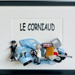 Voiture miniature bleue ancienne avec plusieurs portes et coffre ouverts, figurine en costume blanc au volant et figurine en costume noir coiffée d’un chapeau à côté, sur un fond blanc avec le texte "LE CORNIAUD".