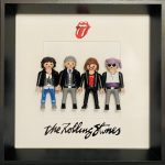 Quatre figurines miniatures représentant les membres du groupe de rock habillés en tenues variées, posées dans un cadre noir avec le logo emblématique des Rolling Stones (bouche rouge avec langue sortie) et le nom du groupe écrit en dessous.