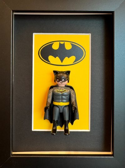 Tableau BATMAN avec figurine Playmobil en costume gris et cape noire devant le logo chauve-souris sur fond jaune