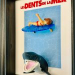 Tableau Les Dents de la mer avec figurine Playmobil sur planche de surf et requin gueule ouverte, cadre bois