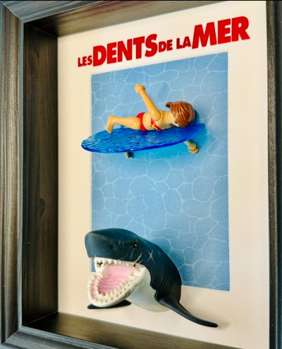 Tableau Les Dents de la mer avec figurine Playmobil sur planche de surf et requin gueule ouverte, cadre bois