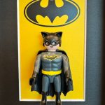 Figurine Playmobil Batman en costume gris et cape noire devant un fond jaune orné du logo chauve-souris