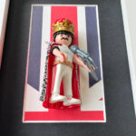Figurine Playmobil Freddie Mercury en tenue blanche, couronne dorée et cape, micro en main sur fond Union Jack