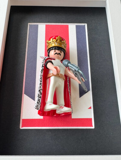 Figurine Playmobil Freddie Mercury en tenue blanche, couronne dorée et cape, micro en main sur fond Union Jack
