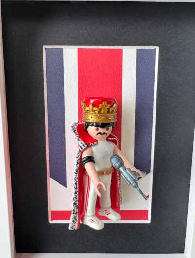 Figurine Playmobil Freddie Mercury avec couronne dorée, cape rouge et micro devant un drapeau britannique