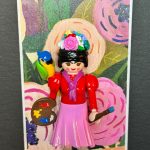Figurine Playmobil inspirée de Frida Kahlo, couronne de fleurs, palette et pinceau, perroquet sur l'épaule, fond floral