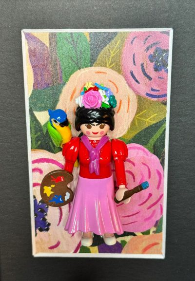 Figurine Playmobil inspirée de Frida Kahlo, couronne de fleurs, palette et pinceau, perroquet sur l'épaule, fond floral