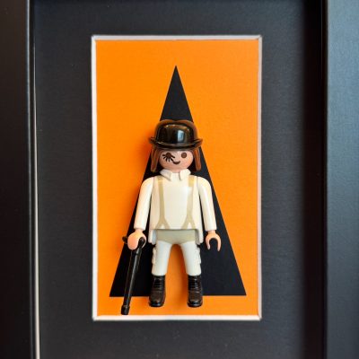 Tableau Orange Mécanique, figurine Playmobil en tenue blanche, chapeau melon, canne et cil peint sur fond orange
