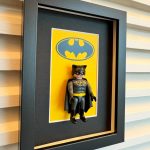 Tableau BATMAN avec figurine Playmobil de Batman sur fond jaune au logo chauve-souris, cadre noir profond au mur
