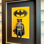 Tableau BATMAN, figurine Playmobil en costume gris et cape noire devant le logo chauve-souris sur fond jaune