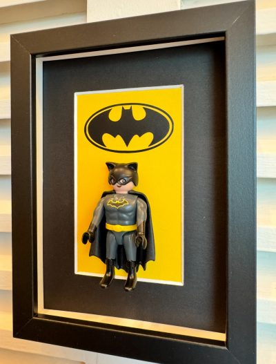 Tableau BATMAN, figurine Playmobil en costume gris et cape noire devant le logo chauve-souris sur fond jaune