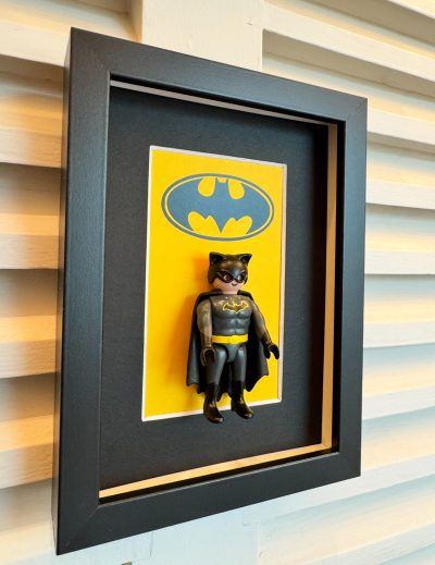 Tableau BATMAN avec figurine Playmobil de Batman sur fond jaune au logo chauve-souris, cadre noir profond au mur
