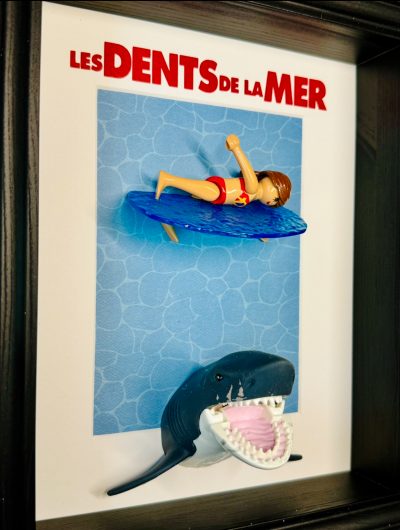 Tableau Les Dents de la mer avec figurine Playmobil surfeuse sur planche bleue et requin gueule ouverte sous elle