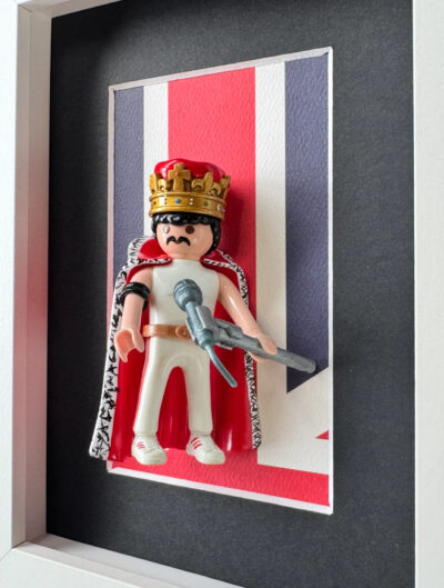 Tableau Freddie Mercury, figurine Playmobil couronnée et cape rouge devant un drapeau britannique, vue en angle