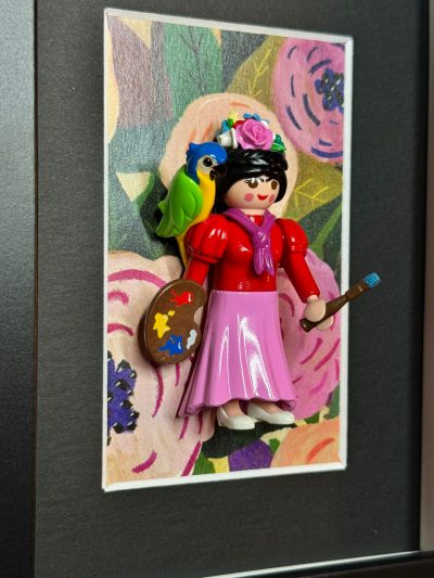 Figurine Playmobil en Frida Kahlo, palette et pinceau, perroquet sur l'epaule, sur fond floral encadre