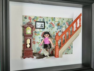 Figurine Playmobil en haut rose et jupe noire passant l'aspirateur près d'un escalier orange, tableau I want to break free