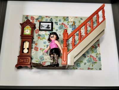 Figurine Playmobil moustachue en haut rose et jupe noire portant un aspirateur près d'un escalier orange, tableau I want to