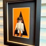 Tableau Orange Mécanique, figurine Playmobil en tenue blanche et chapeau melon sur fond orange, cadre noir
