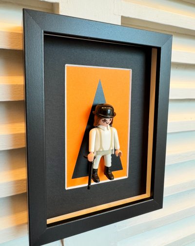 Tableau ORANGE MÉCANIQUE, figurine Playmobil en tenue blanche et chapeau melon sur fond orange dans un cadre noir