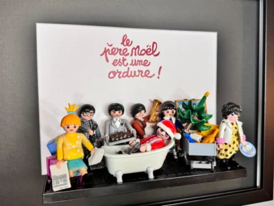 Tableau Le Père Noël est une ordure avec figurines Playmobil autour d'une baignoire et titre calligraphié en rouge