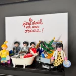 Tableau Le Père Noël est une ordure avec figurines Playmobil, titre manuscrit rouge et personnage en costume rouge dans une