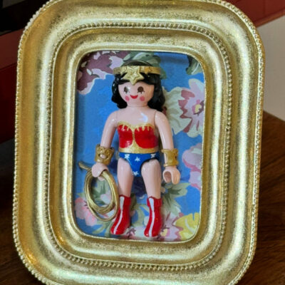 Figurine Playmobil Wonder Woman avec lasso doré et diadème étoilé, encadrée dans un cadre doré sur fond fleuri bleu