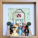 Tableau Bridgerton avec figurines Playmobil en robes de bal devant une facade fleurie, cadre en bois clair
