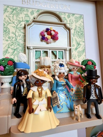 Detail du tableau Bridgerton, figurines Playmobil en robes et hauts-de-forme devant un decor floral vert d'eau