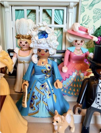 Figurine Playmobil de la Reine Charlotte en robe bleue et perruque fleurie, entourée de dames et d'un petit chien