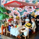 Scène du Déjeuner des canotiers recréée en figurines Playmobil sous un store rayé rouge, table dressée et fond fleuri