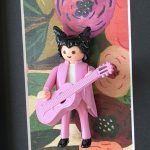 Figurine Playmobil en costume rose avec guitare rose devant un fond fleuri, œuvre Matthieu Chedid