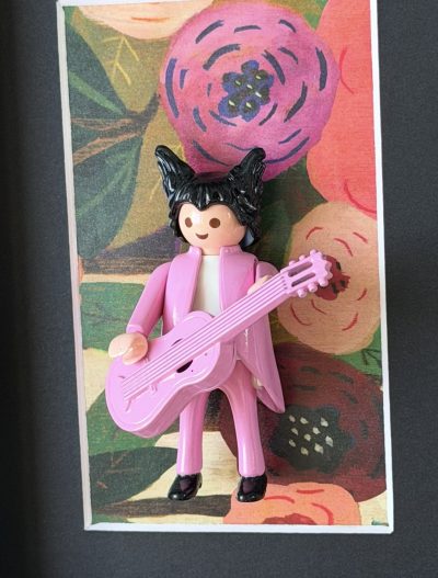 Figurine Playmobil en costume rose avec guitare rose devant un fond fleuri, œuvre Matthieu Chedid