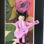 Figurine Playmobil en costume rose jouant d'une guitare rose devant un fond floral, tableau Matthieu Chedid