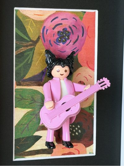 Figurine Playmobil en costume rose jouant d'une guitare rose devant un fond floral, tableau Matthieu Chedid