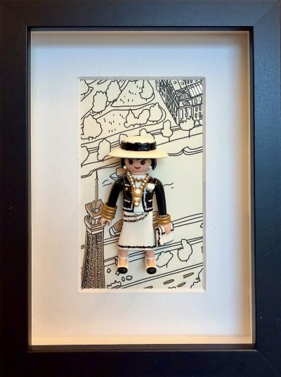 Tableau Coco Chanel représentant Gabrielle Chanel en noir et ivoire devant un dessin de Paris, dans un cadre noir.