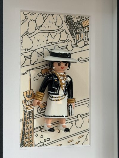Portrait de Gabrielle Chanel vu de biais, montrant le volume du chapeau, les bijoux et le sac devant la tour Eiffel dessinée.