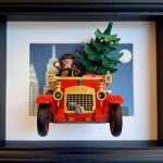 Tableau de Noël avec voiture ancienne rouge, conducteur et sapin devant une ville nocturne, dans un cadre noir.
