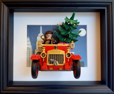 Tableau de Noël avec voiture ancienne rouge, conducteur et sapin devant une ville nocturne, dans un cadre noir.