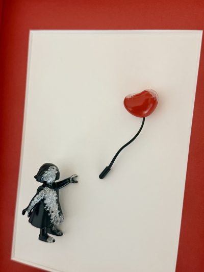 Détail de la main tendue, des touches blanches sur la figurine noire et du ballon cœur rouge.