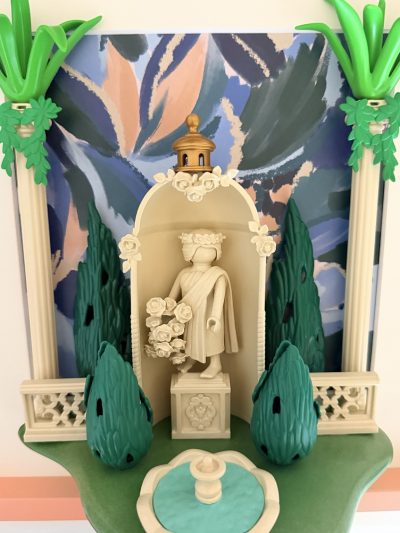Statue ivoire couronnée de fleurs dans une alcôve ornée de roses, entre cyprès et colonnes, avec fontaine au premier plan.