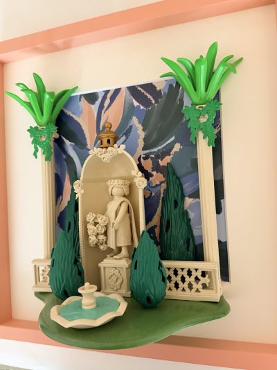 Vue oblique du jardin de Villa Médicis, avec fontaine turquoise au premier plan, statue dans une alcôve et colonnes claires.