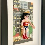 Wonder Woman vue de biais avec lasso doré, bracelets, bustier rouge et tenue bleue étoilée devant des immeubles dessinés.